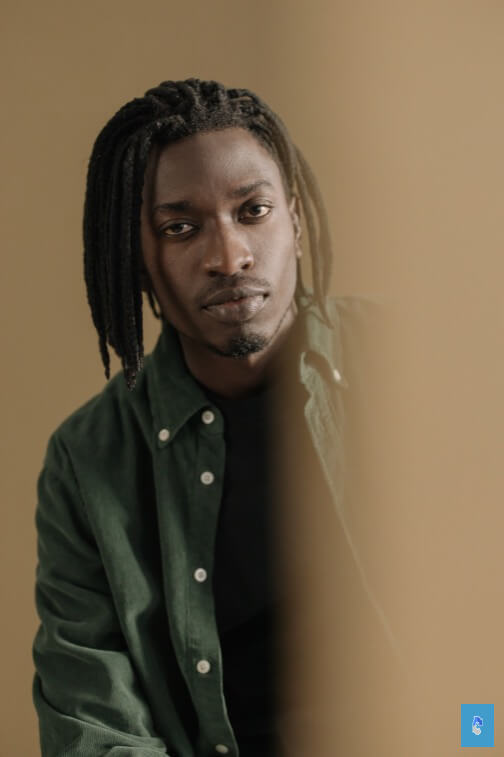 Person with braided hair in green shirt and black top, partially obscured by blurred element.