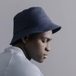 Person in profile with blue bucket hat and light shirt against a neutral background.