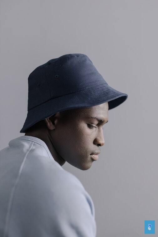 Person in profile with blue bucket hat and light shirt against a neutral background.