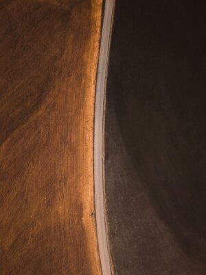 Aerial view of road dividing brown and dark fields, indicating different vegetation stages.