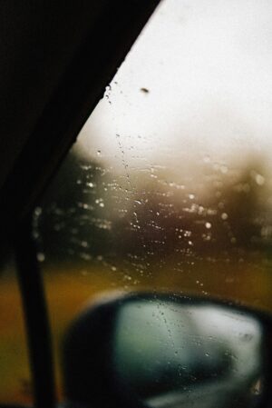 Car side window with raindrops, blurred side mirror, and soft focus background.