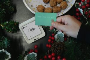 Person holds a green credit card at a contactless terminal; festive decor and walnuts present.