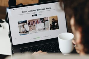 Person using a laptop with a business tools webpage, holding a white mug.