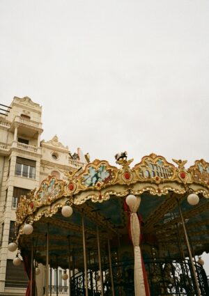 Vintage carousel near intricate building under overcast sky.