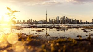 City skyline with tall buildings and tower across water at sunset with reflections.