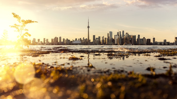 City skyline with tall buildings and tower across water at sunset with reflections.
