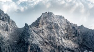 Rocky mountain peaks with steep slopes under a partly cloudy sky.