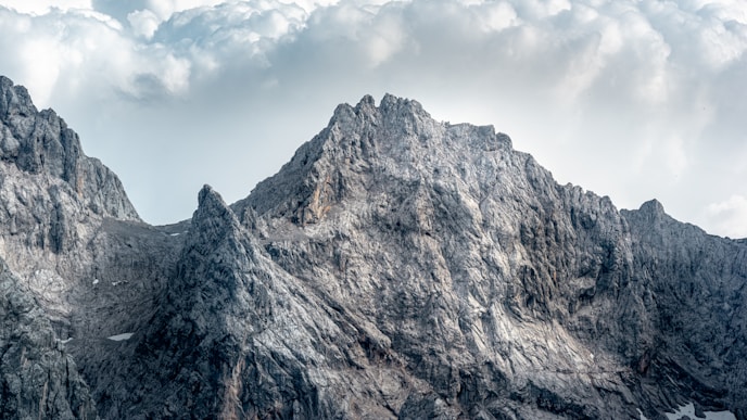 Rocky mountain peaks with steep slopes under a partly cloudy sky.