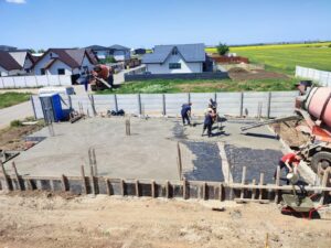 Construction workers pouring and spreading concrete on a foundation with rebar and mixer truck.