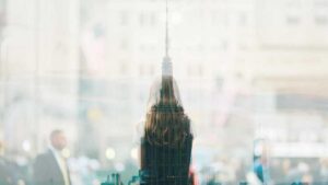 Double exposure of a woman with long hair seen from behind and a city skyline with tall buildings.